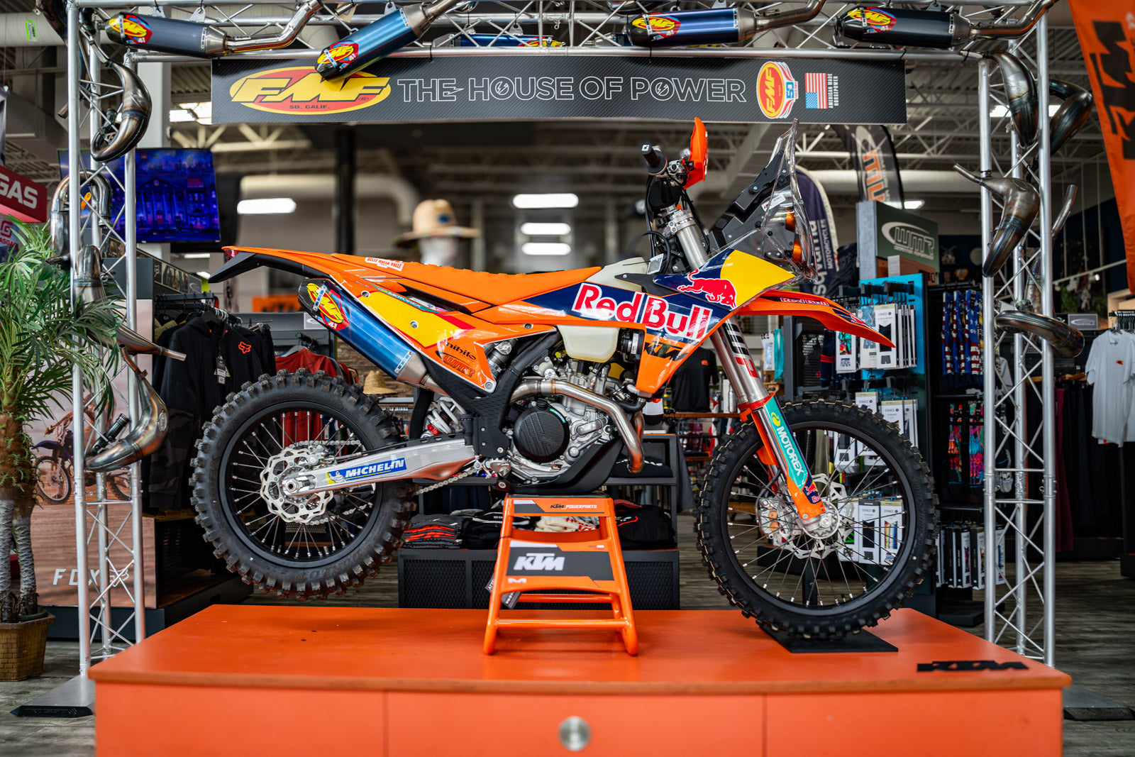 KTM Orange and blue dirt bike on display with 'Red Bull' branding in a showroom setting in the FMF House of Power Zone